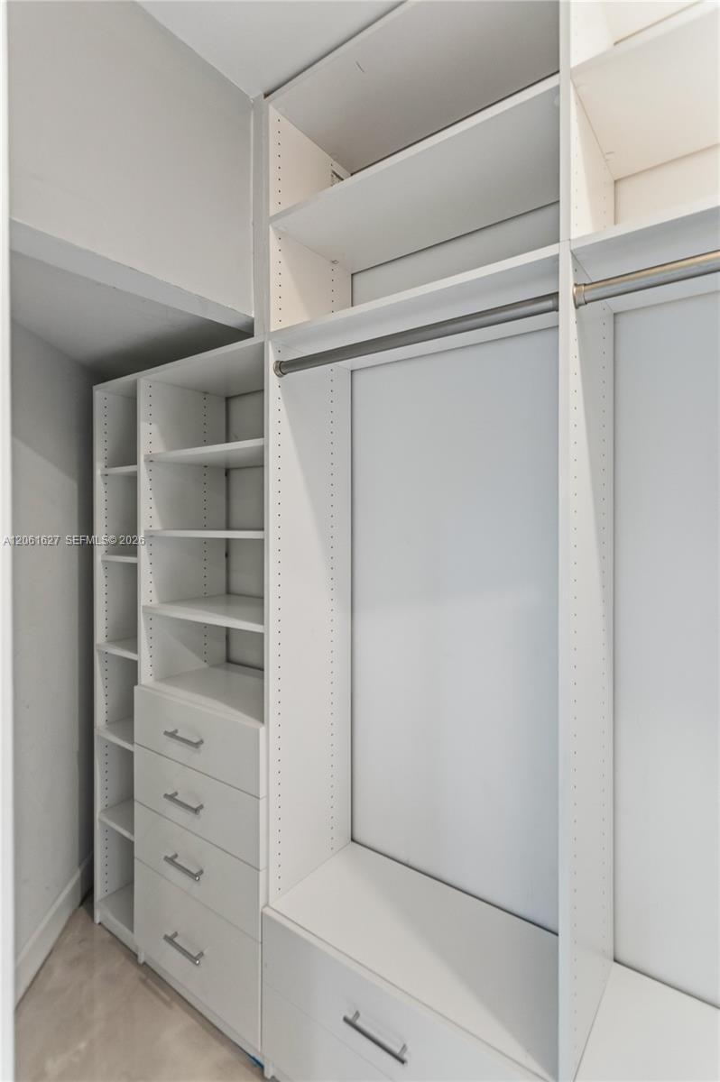 Custom built-in closet organization system featuring white cabinetry, adjustable shelving, integrated garment rods, and four pull-out drawers with met