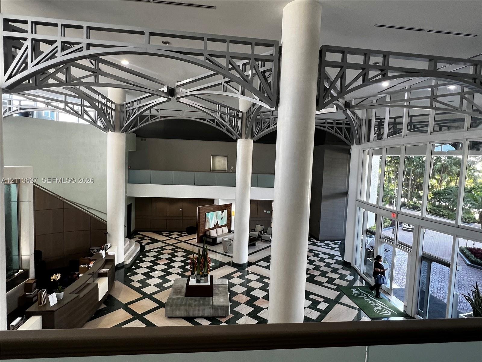 Grand foyer featuring vaulted structural steel ceiling trusses, floor-to-ceiling windows, polished stone flooring in a geometric pattern, and prominen