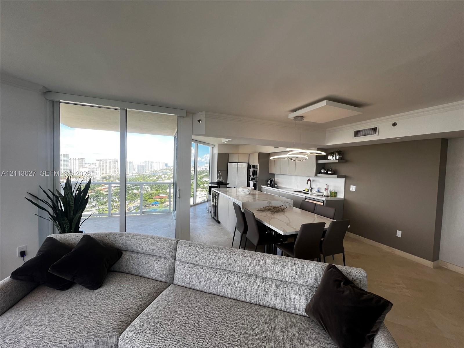 Open-concept kitchen featuring an oversized island with stone-finish countertops, flat-panel cabinetry, built-in stainless steel appliances, and floor