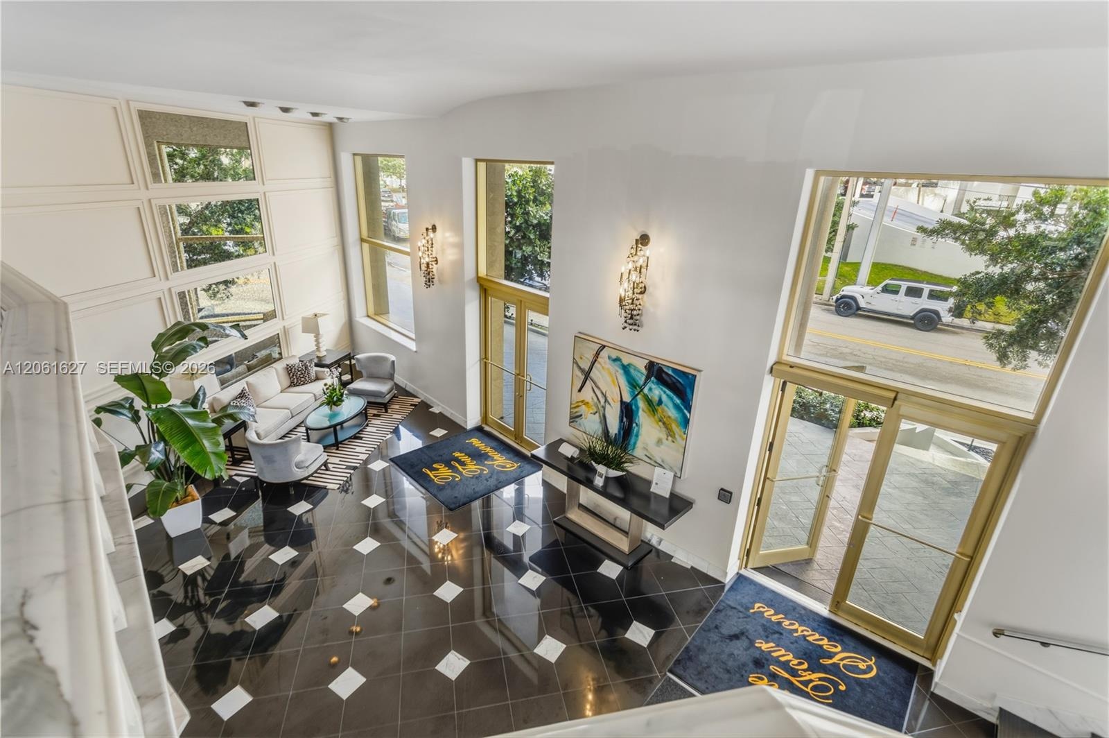 Double-height foyer featuring high-gloss geometric tile flooring, floor-to-ceiling windows, custom wall paneling, and metallic wall-mounted sconces