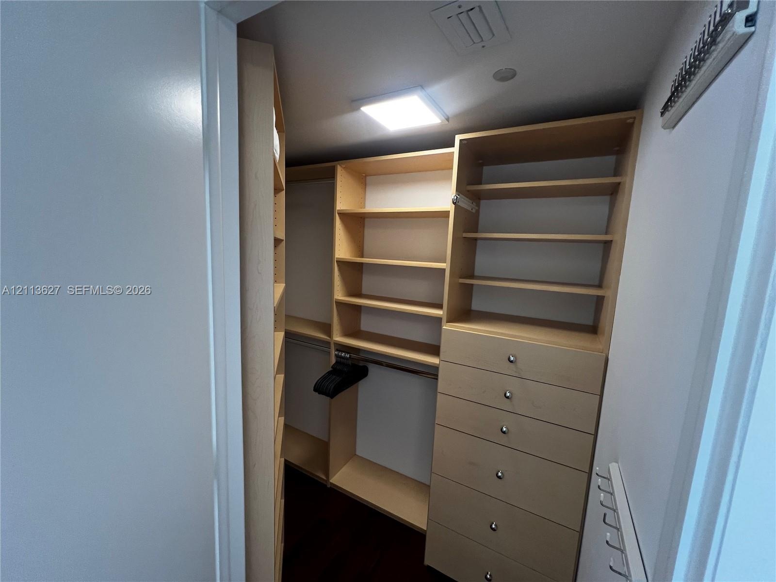 Custom walk-in closet featuring light-toned wooden shelving, integrated drawer stack with metal hardware, and recessed lighting