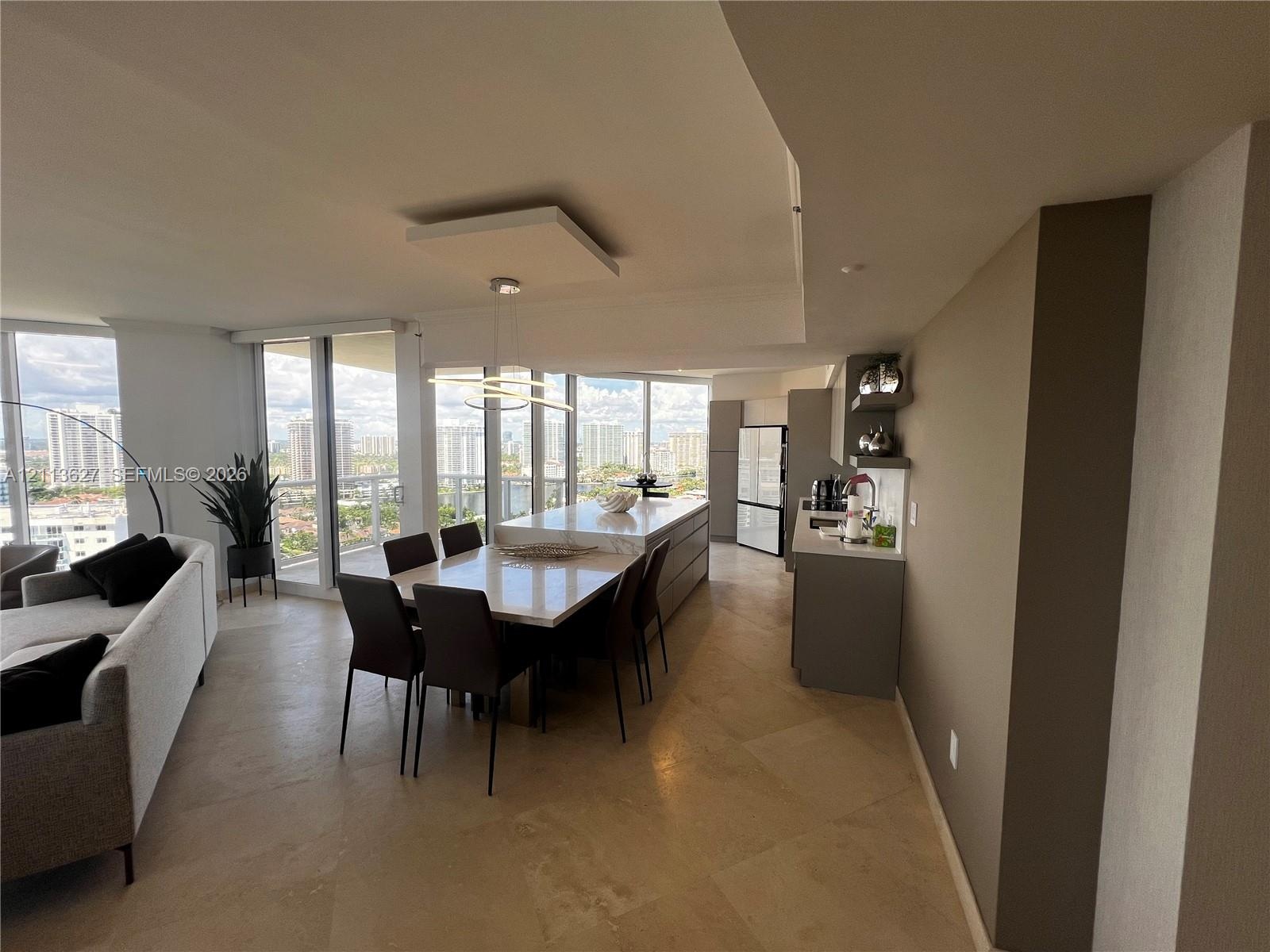 Open-concept kitchen and dining area featuring large-format stone flooring, floor-to-ceiling windows, center island with stone countertop, and built-i