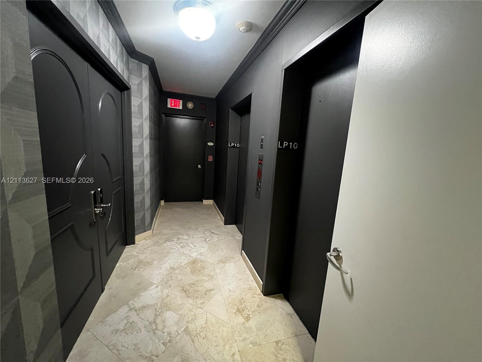 Stone tile flooring, geometric textured wall covering, double-door entry with metallic hardware, dual elevator access, and monochromatic architectural