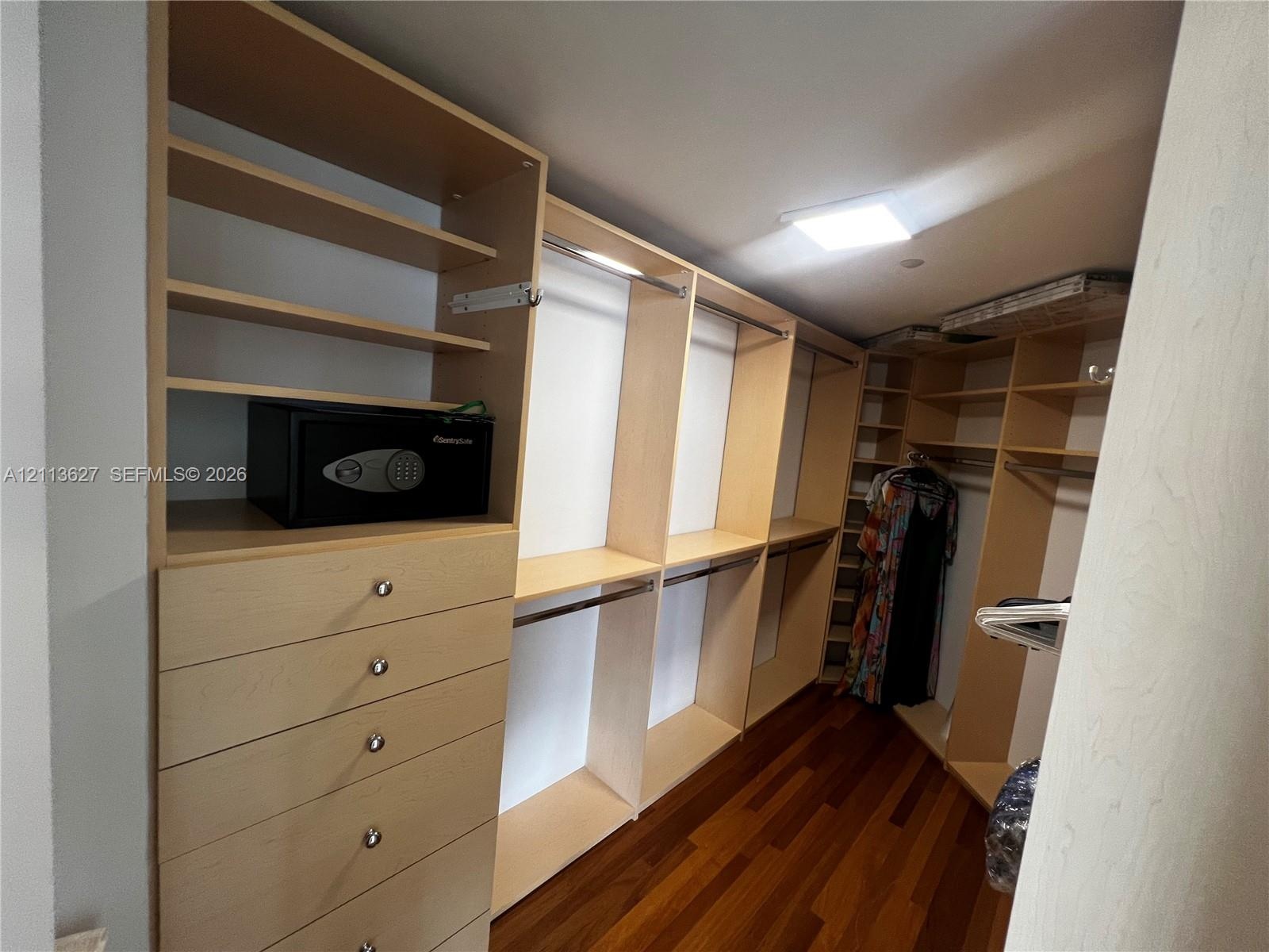 Walk-in closet featuring custom light-finish wood cabinetry, integrated shelving units, multiple storage drawers, and wood-finish flooring