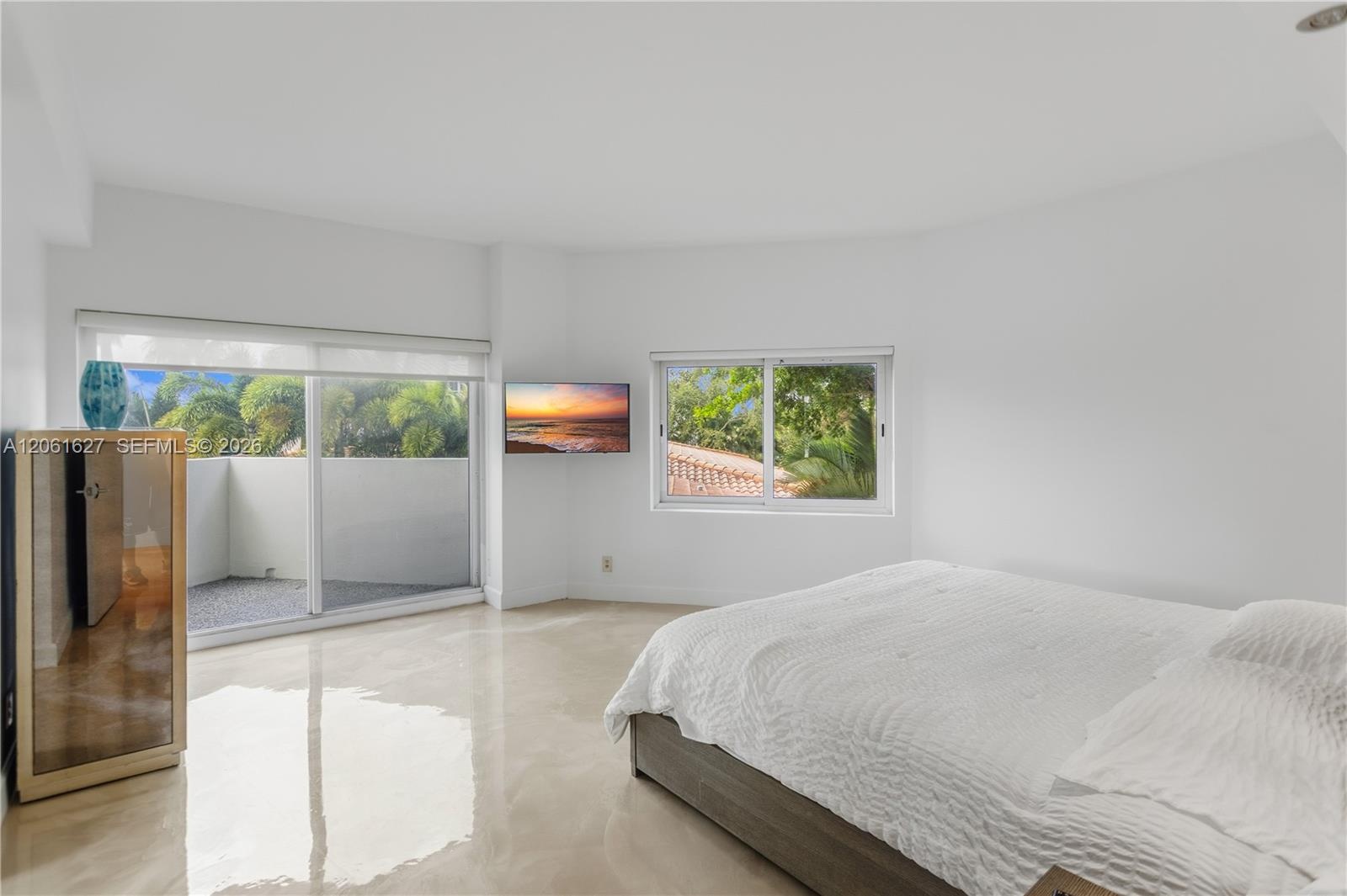 Polished concrete flooring, sliding glass door with access to a private balcony, and dual windows with exterior greenery