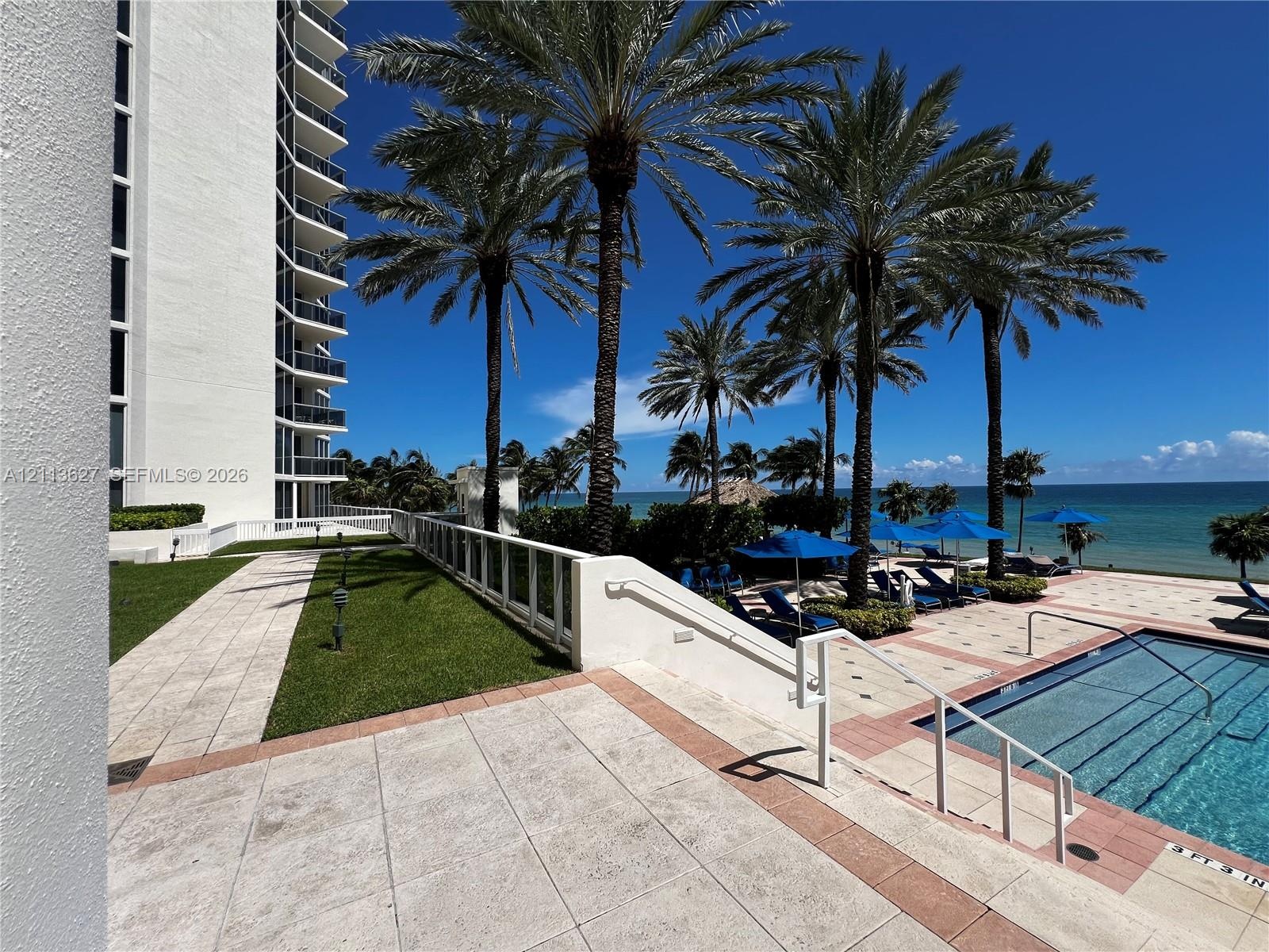 Outdoor swimming pool with tile decking, manicured lawn, palm trees, and barrier railing