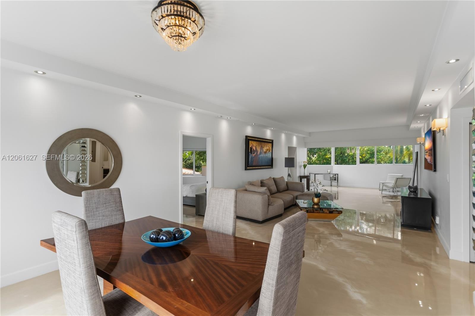 Open-concept living space featuring high-gloss flooring, recessed lighting, a decorative tiered chandelier, and expansive windows