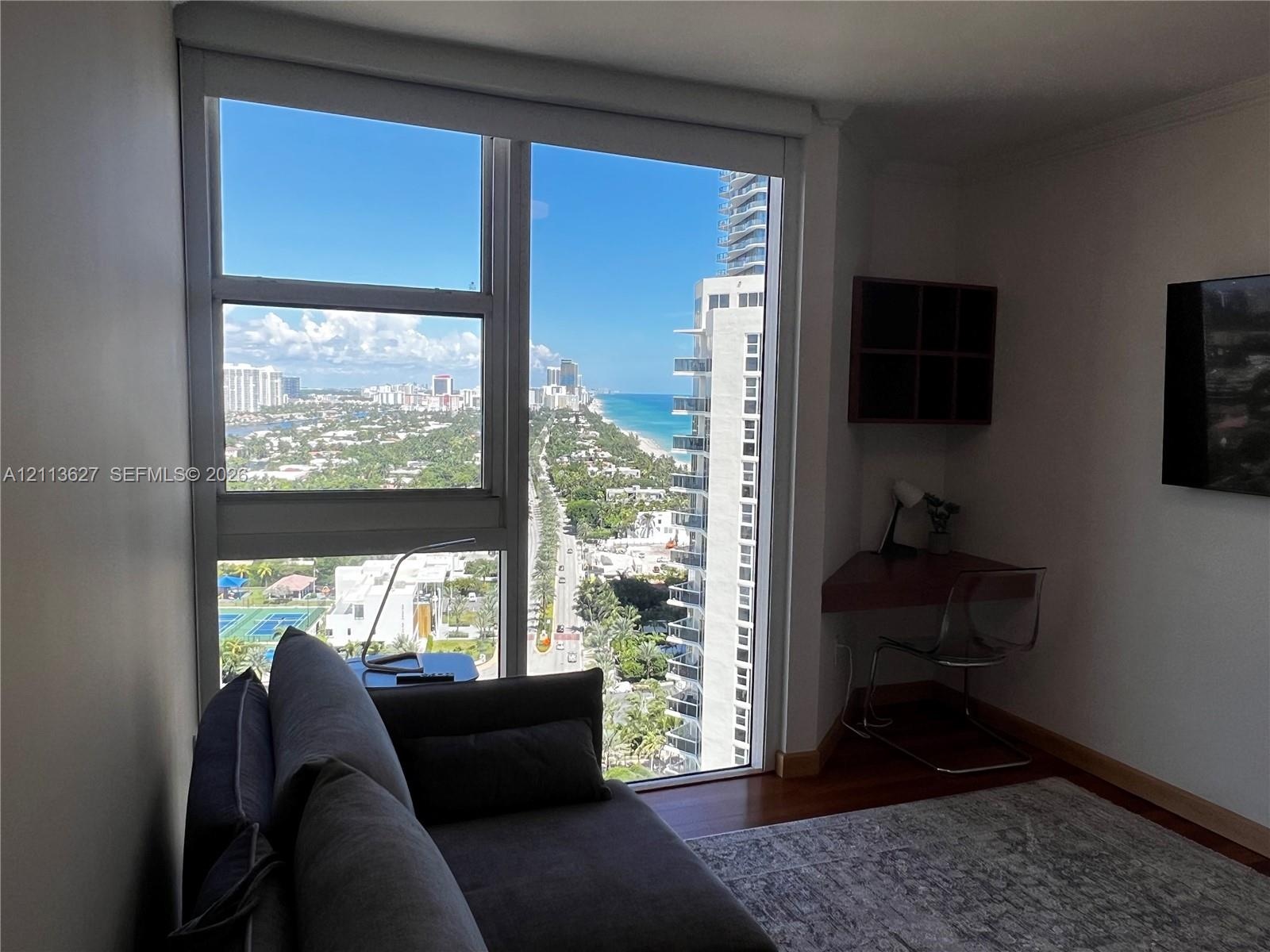 Floor-to-ceiling windows featuring coastal and urban skyline scenery, hardwood flooring, and a built-in corner desk