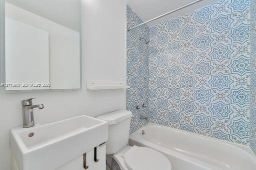 Bathroom featuring a vanity with a rectangular basin, metallic faucet, wall-mounted mirror, and a shower-tub combination accented with patterned tile 