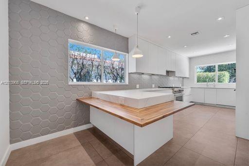 Kitchen featuring matte white flat-panel cabinetry, hexagonal-patterned accent wall, stone-topped island with wood-finished breakfast bar, and tile fl