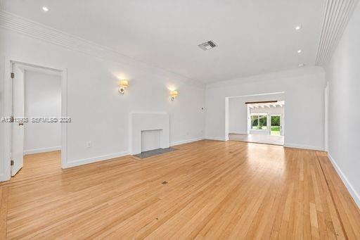 Living area featuring wood-finish flooring, a decorative fireplace, recessed ceiling lighting, wall-mounted sconces, and crown molding
