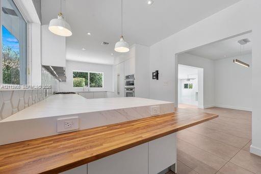 Kitchen featuring a waterfall-edge countertop, butcher block peninsula, geometric tiled backsplash, recessed lighting, and stainless steel built-in do