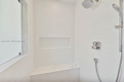 Walk-in shower featuring white subway-style wall tile, a stone-finish bench seat, an integrated wall niche, and dual-function polished chrome shower f