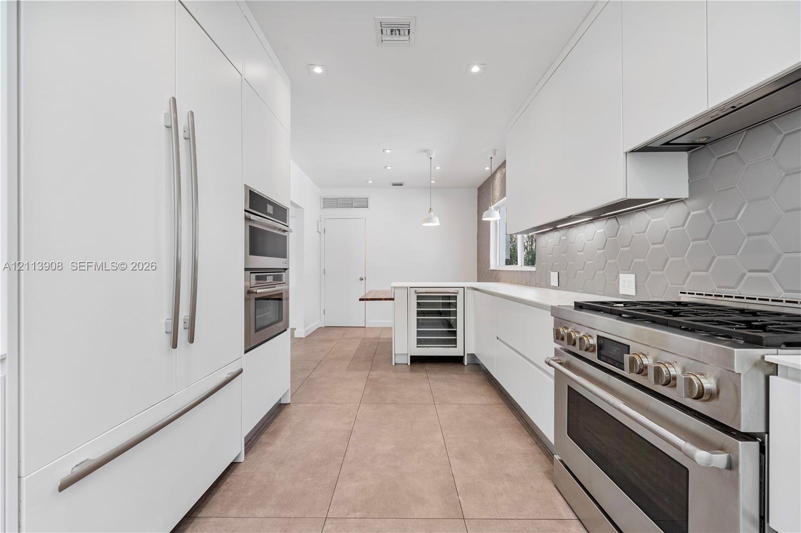 Contemporary kitchen featuring flat-panel white cabinetry, stainless steel professional-grade range, hexagonal tile backsplash, built-in wine refriger