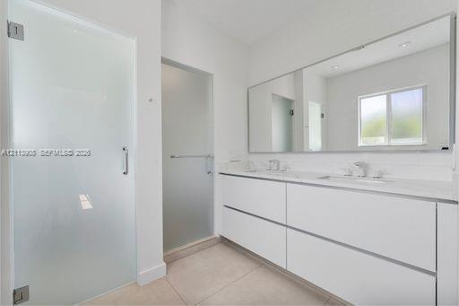 Bathroom featuring a dual-sink floating vanity with white cabinetry, a full-width wall mirror, oversized tile flooring, and frosted glass door enclosu