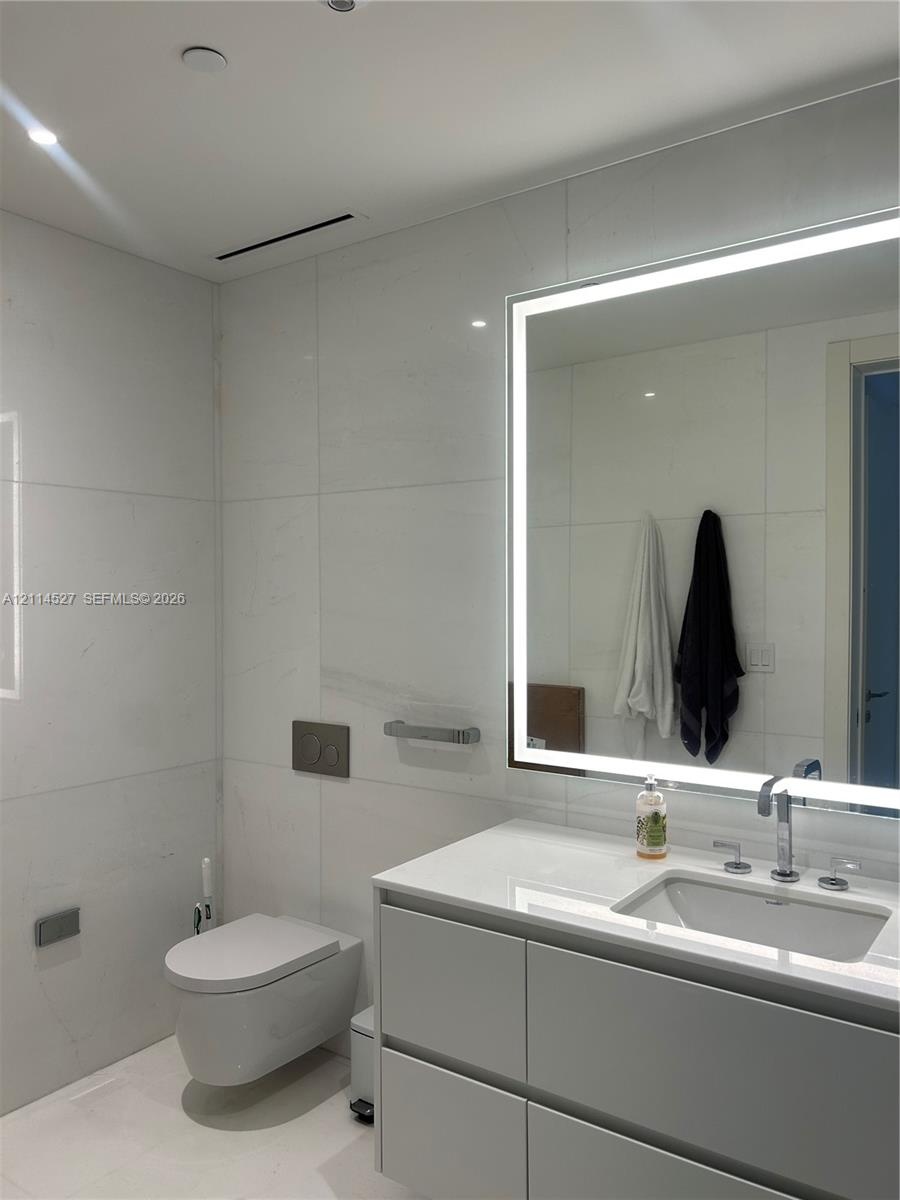Wall-mounted toilet with a dual-flush actuator plate, large-format tile wall cladding, modern floating vanity with a seamless countertop, rectangular 