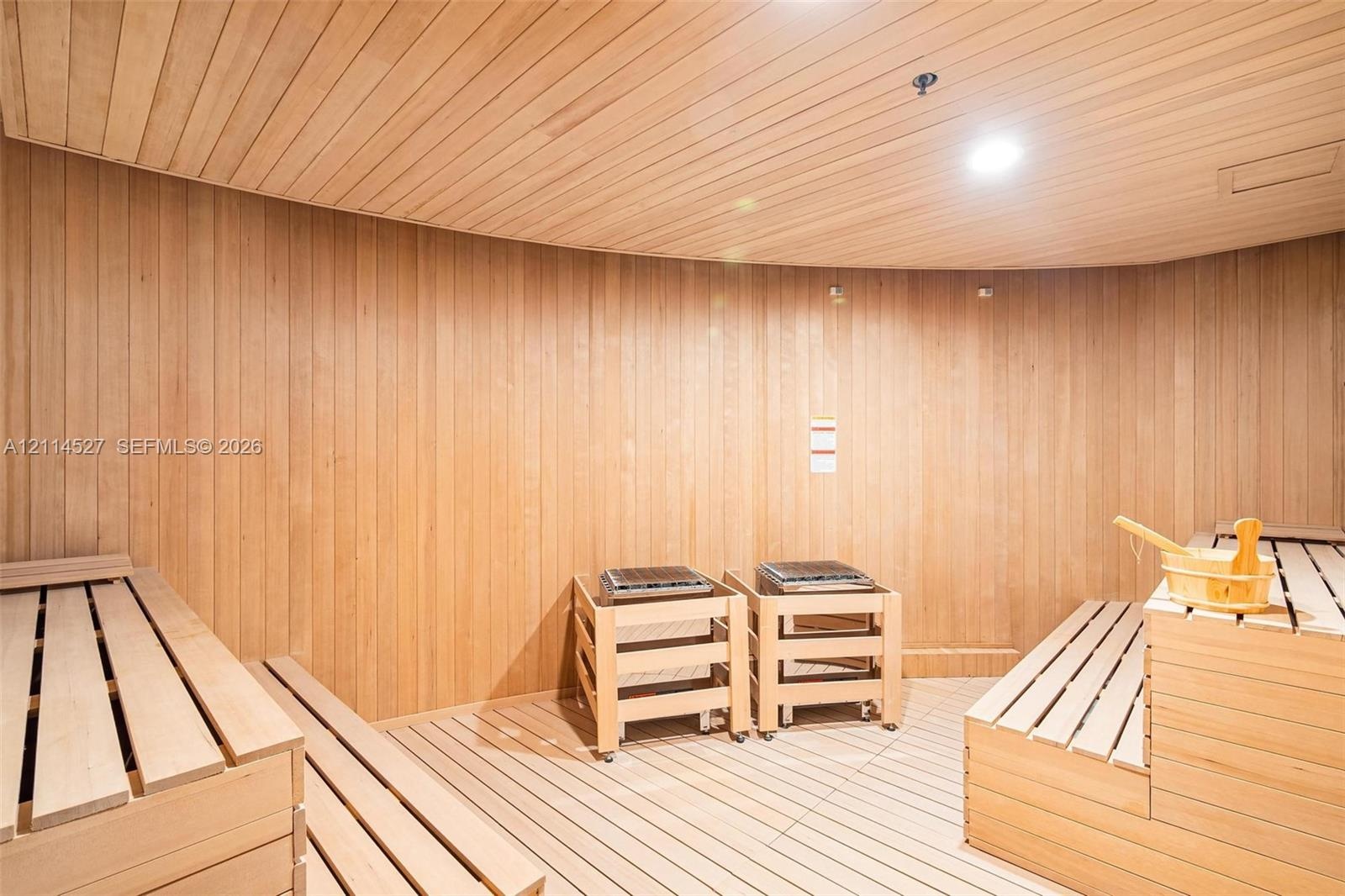 Sauna featuring wood-paneled walls and ceiling, tiered slatted wood benches, and dual built-in heating units