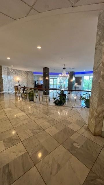 Polished stone flooring throughout, expansive wall-to-wall stone cladding, central chandelier, and decorative metal balustrade with a wooden handrail