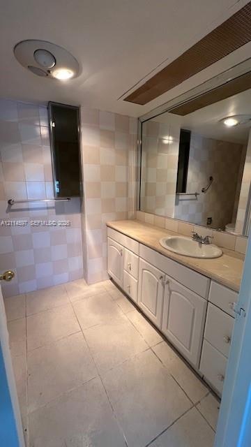 Bathroom featuring a vanity with white cabinetry, a neutral countertop, an oval under-mount sink, a full-width wall mirror, and checkered wall tile