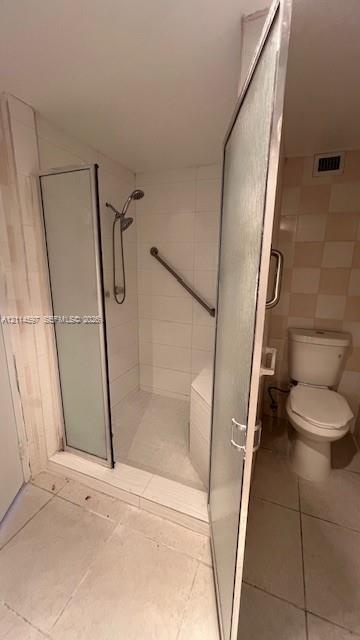 Walk-in shower enclosure featuring a handheld showerhead, integrated seating, and mounted grab bar, finished with white wall tiling and a standard toi