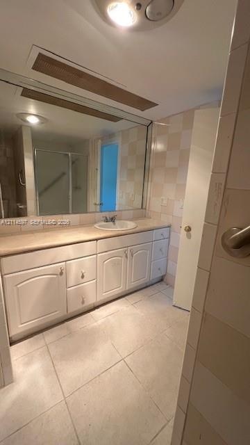Bathroom featuring a large vanity with white cabinetry, integrated sink, and stone-surface countertop, complemented by floor-to-ceiling wall tiles and