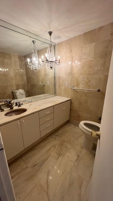 Bathroom featuring full-wall tile surround, vanity with inset sink and stone countertop, large-format tiled flooring, and a decorative crystal chandel