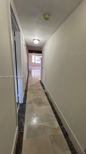 Hallway featuring stone tile flooring with decorative dark stone borders, flush-mount ceiling lighting, and louvered closet doors