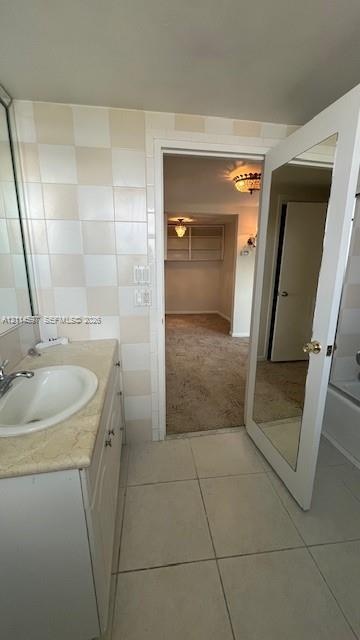 Bathroom featuring a vanity with an integrated basin, neutral stone-finish countertop, full-height wall tiling, and a door with an inset full-length m