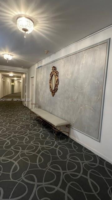 Hallway featuring patterned wall-to-wall carpeting, decorative ceiling-mounted crystal fixtures, and a recessed wall panel with textured finish