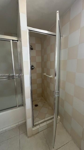 Walk-in shower enclosure featuring a chrome-framed hinged door, wall-mounted shower head, integrated towel bar, and checkerboard-patterned tile wall s