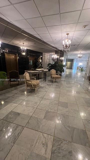 Large-format stone flooring, wall-spanning mirror, and multi-arm chandelier fixtures in a high-ceiling lobby