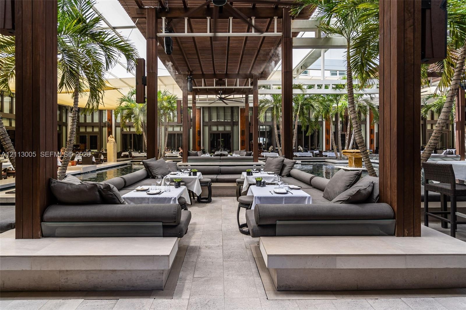 Covered outdoor patio featuring a timber pergola, integrated stone seating platforms, natural stone flooring, and mature palm trees