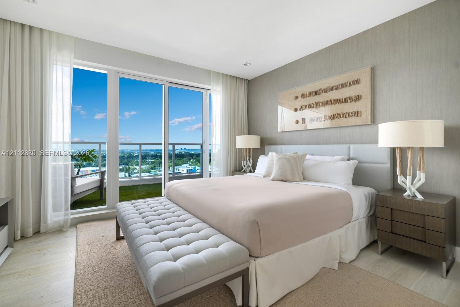 Floor-to-ceiling sliding glass door, private balcony with metal railing, neutral textured accent wall, and recessed ceiling lighting