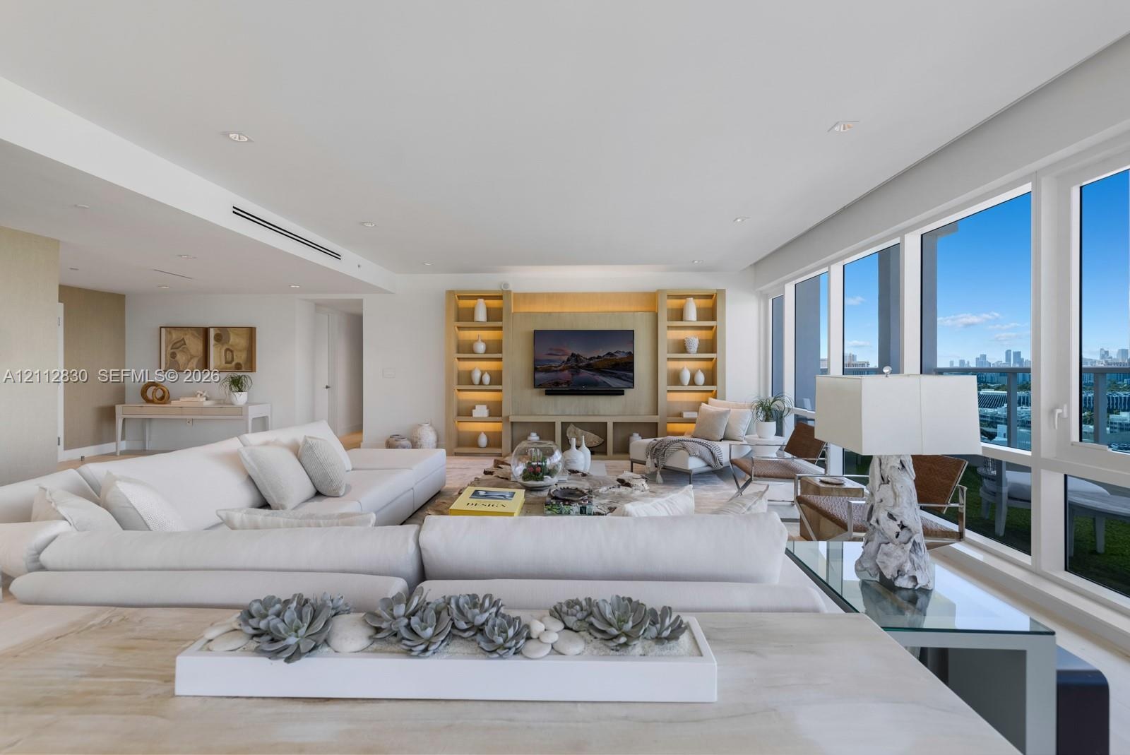 Open-concept interior featuring floor-to-ceiling windows, custom built-in cabinetry with integrated shelving, recessed lighting, and smooth-finish wal