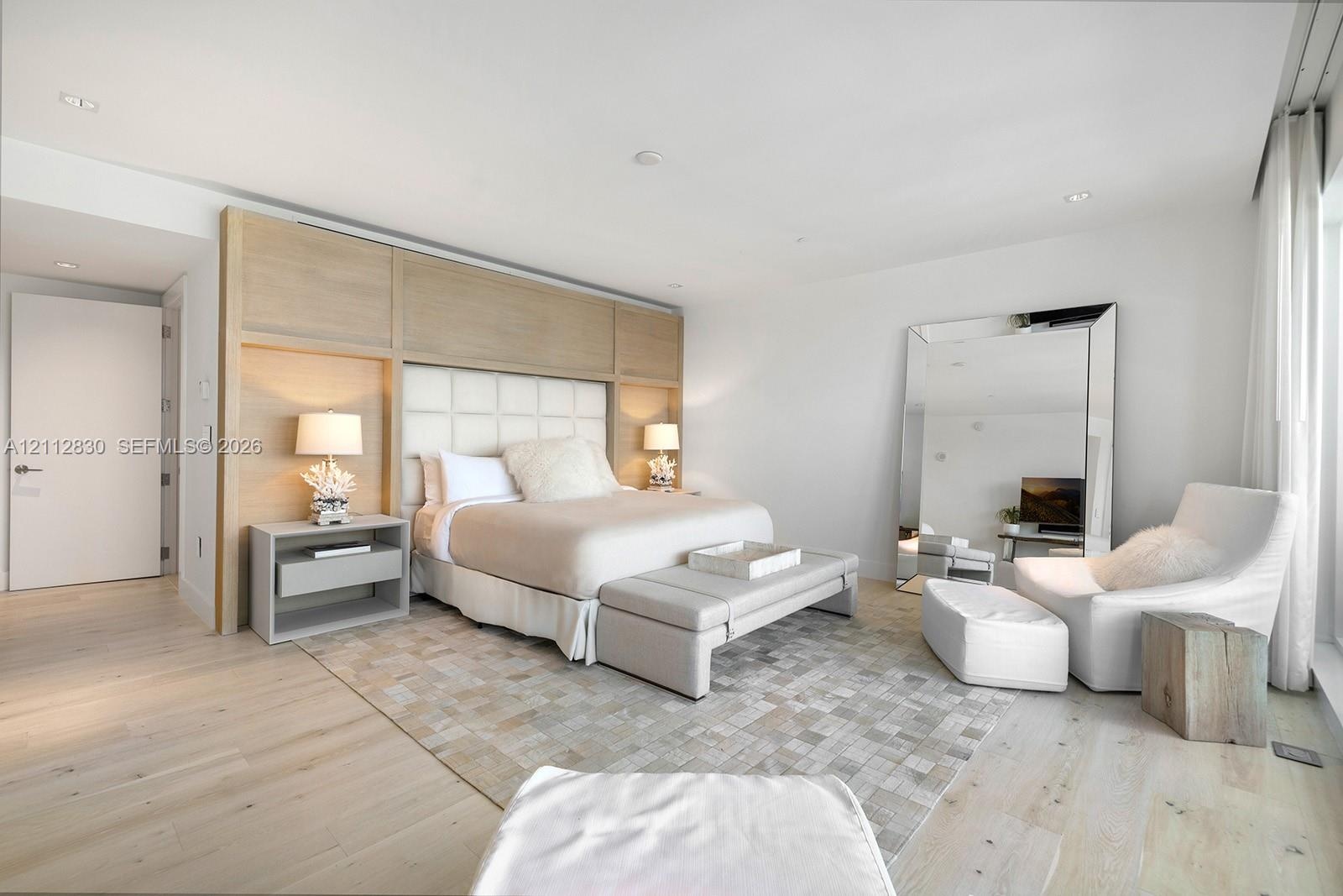 Light-toned wood-finish flooring, custom built-in wood-panel headboard with integrated lighting, and recessed ceiling lighting