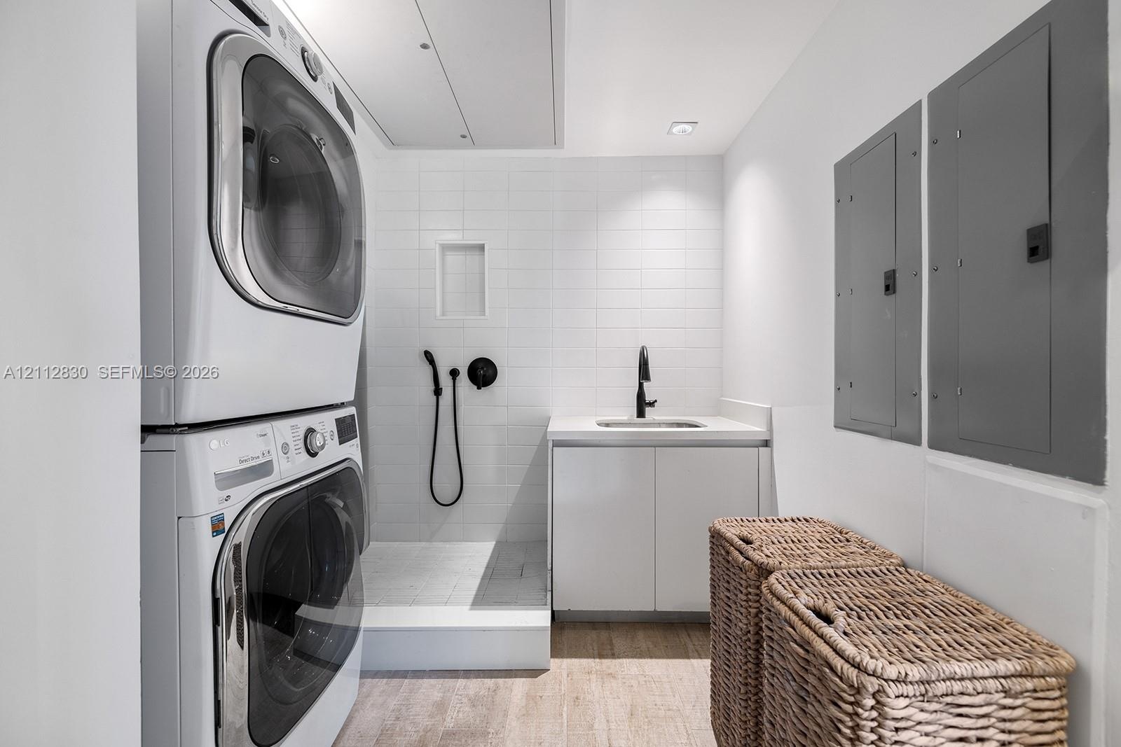 Utility room featuring stackable laundry appliances, a tiled walk-in shower with matte black fixtures, a white vanity with an integrated sink, and rec