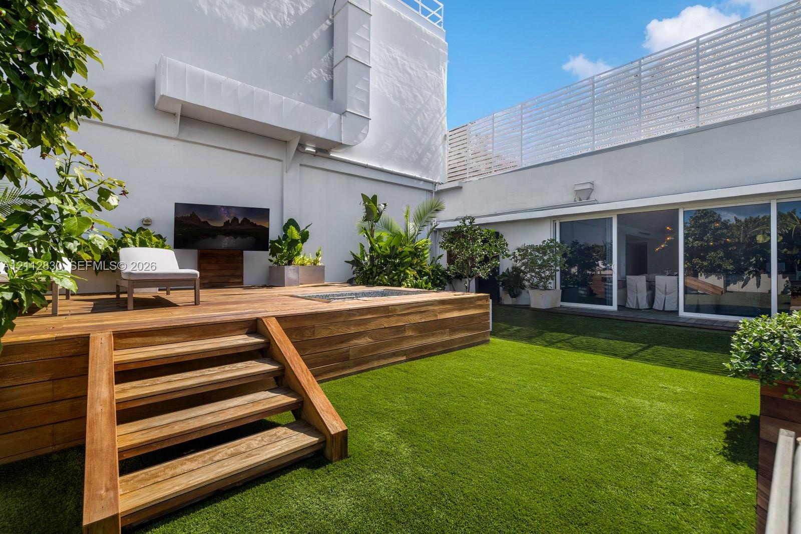 Outdoor courtyard featuring a multi-level wood deck, built-in recessed fire feature, synthetic lawn, and perimeter privacy fencing