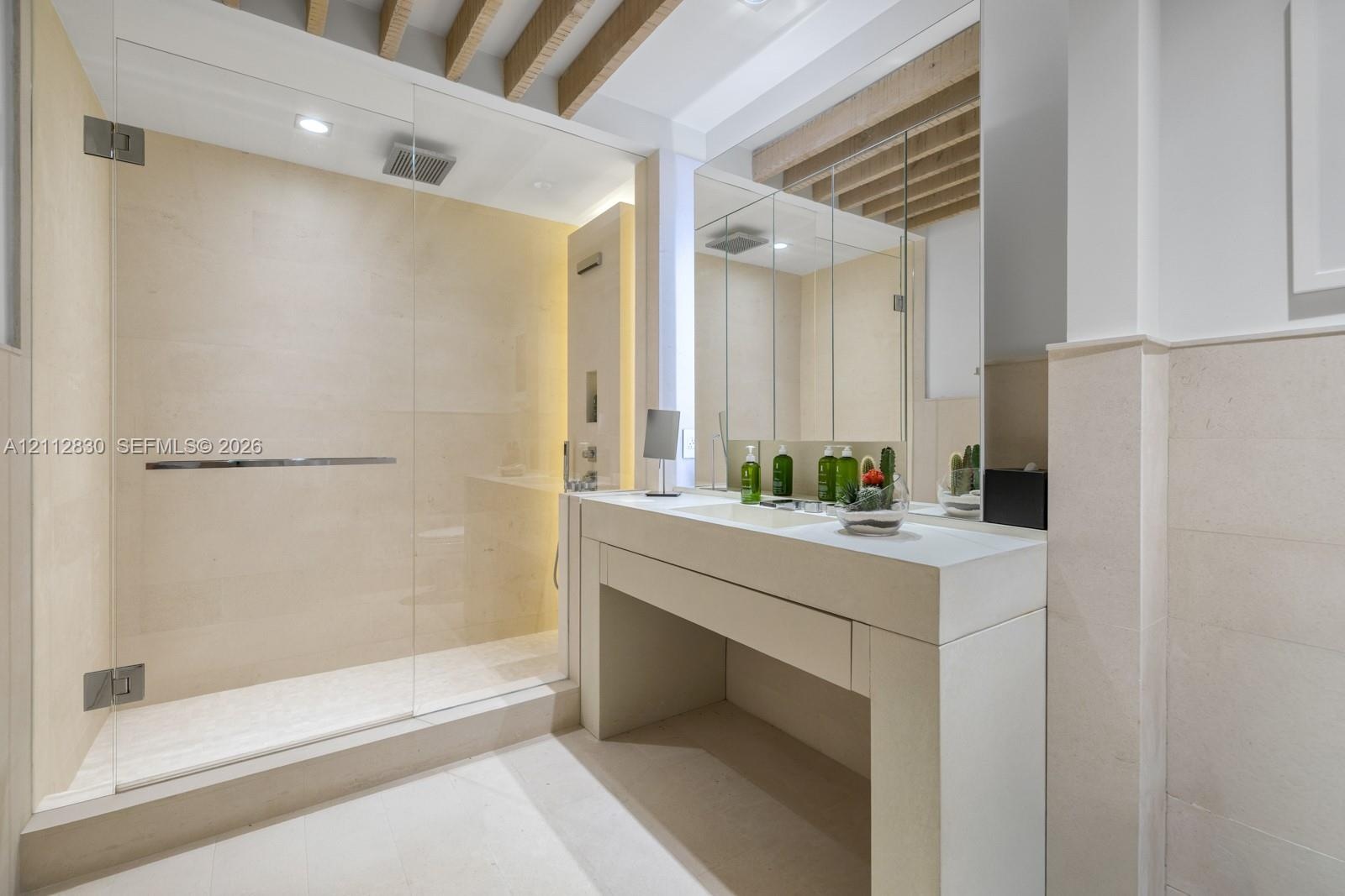Stone-tiled shower featuring a frameless glass enclosure and rainfall showerhead, complemented by a custom stone vanity with an integrated sink and re