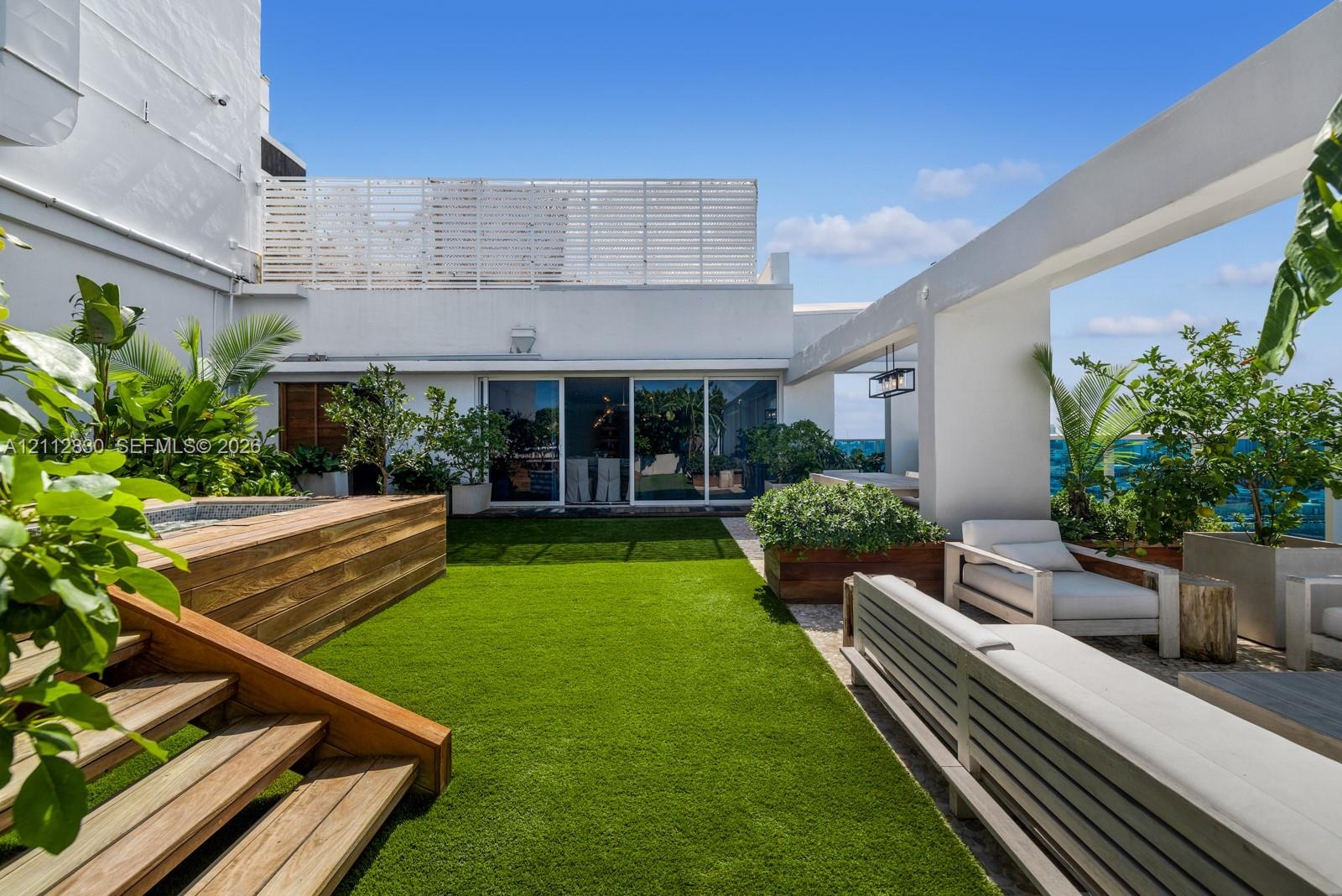 Rooftop terrace featuring artificial turf, tiered wood-finish stairs, a recessed spa, a pergola structure, and built-in wood-finish planters