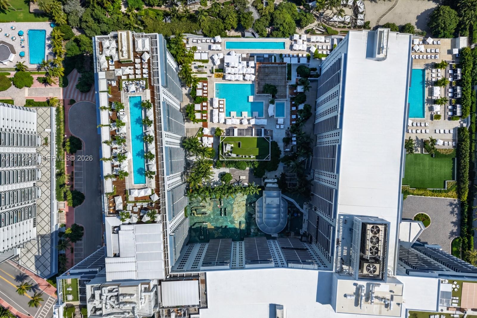 Aerial perspective of a multi-structure complex featuring multiple rectangular swimming pools, hardscaped recreation areas, integrated green space, an
