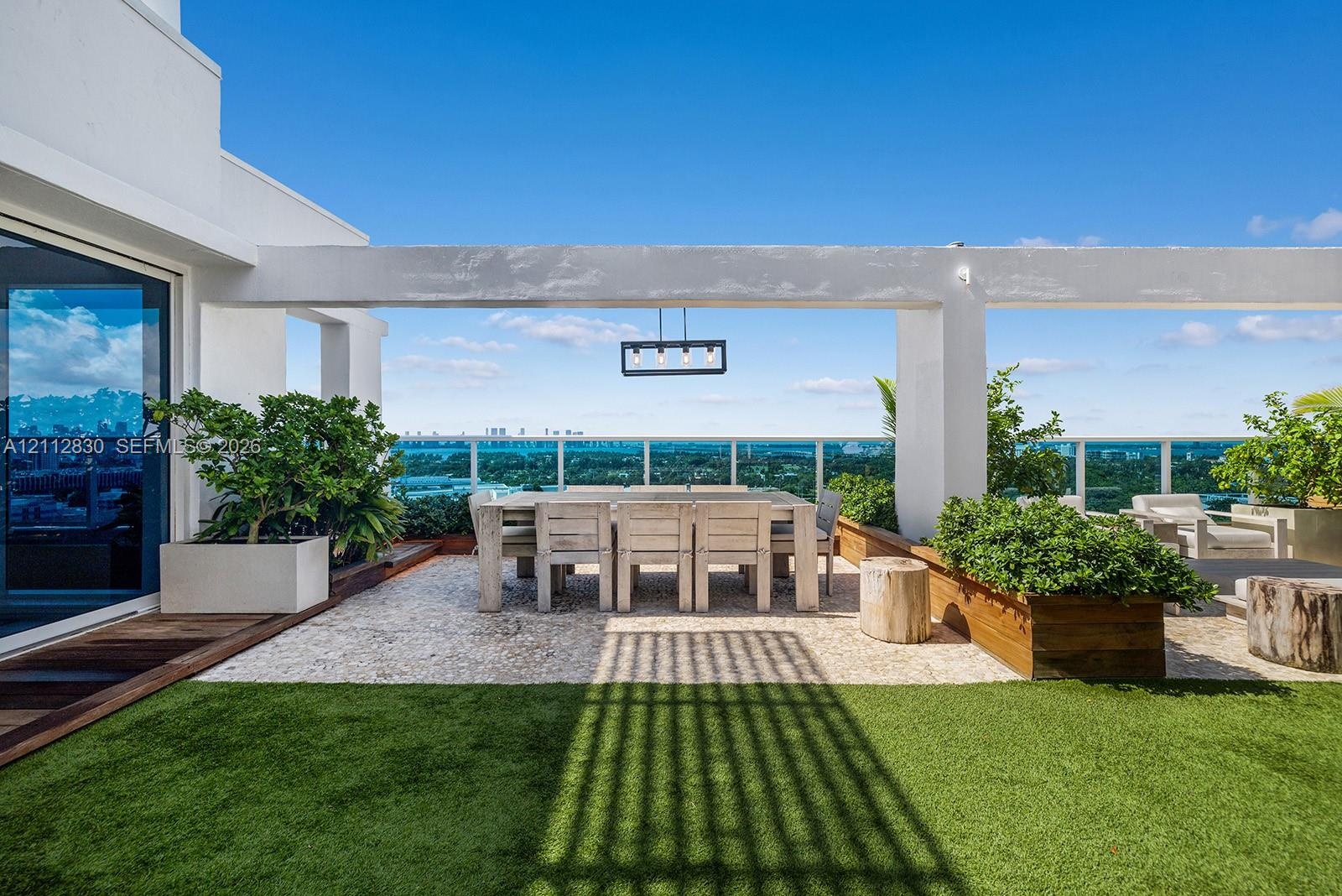 Rooftop terrace featuring synthetic turf, stone-paver flooring, a built-in pergola, integrated planter boxes, and a linear pendant light fixture