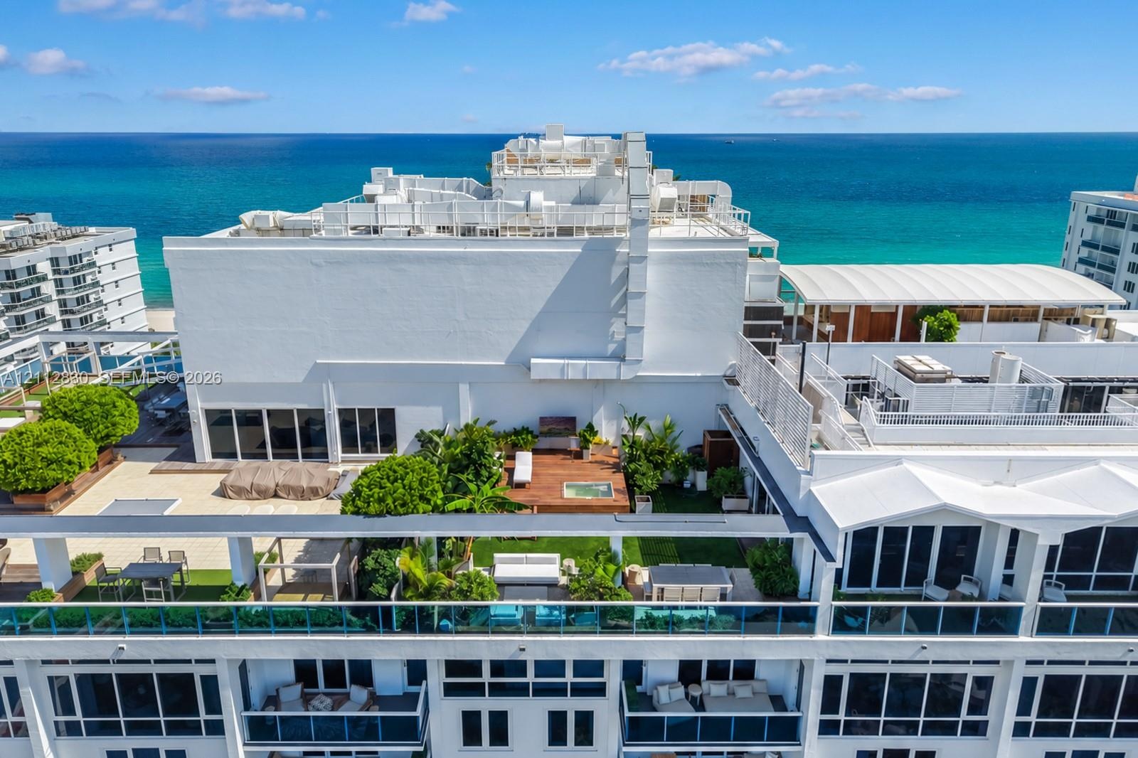 Rooftop terrace featuring wood decking, built-in hot tub, landscaping, glass railings, and ocean backdrop