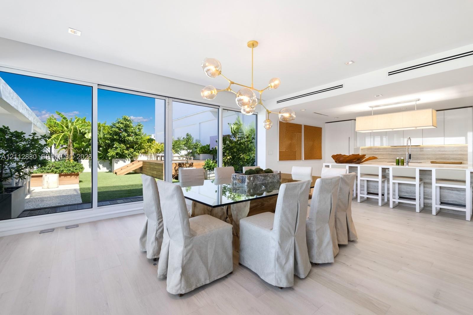 Floor-to-ceiling sliding glass panels, wood-finish flooring, linear recessed lighting, brass-finish multi-arm chandelier, and white flat-panel cabinet