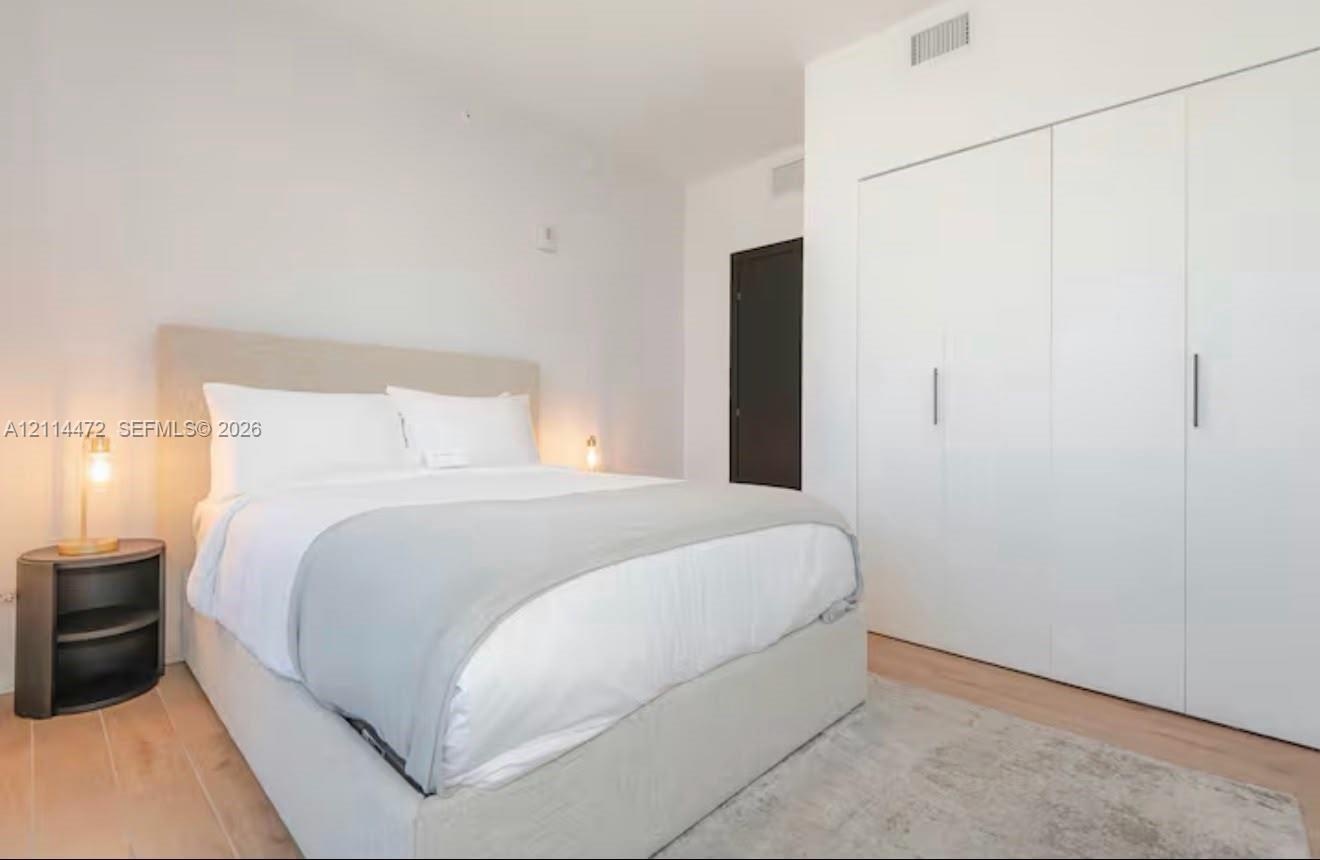 Room featuring smooth-finish white walls, light-toned wood-finish flooring, and built-in floor-to-ceiling storage cabinetry with vertical metallic har