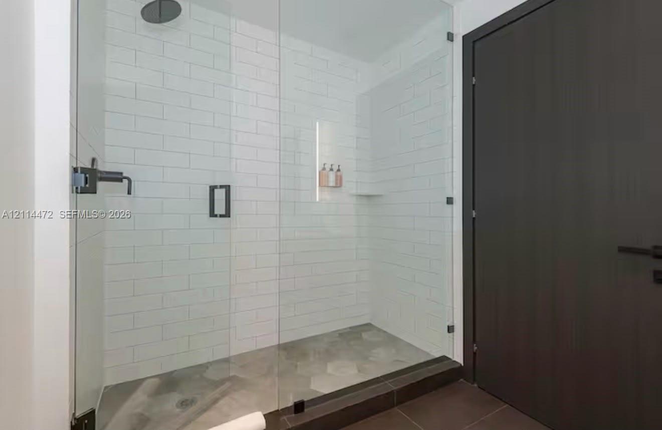 Walk-in shower featuring a frameless glass enclosure, white subway tile surround, hexagonal tile flooring, matte black rainfall showerhead, and integr