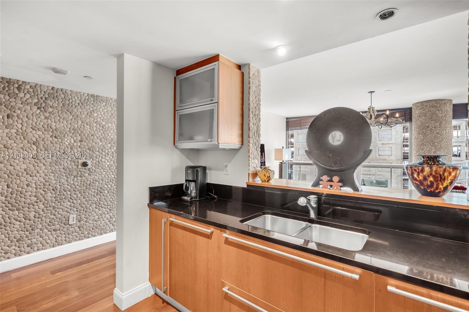 Kitchen area featuring wood cabinetry, dark stone countertops, an integrated double-basin stainless steel sink, frosted glass upper cabinets, and a de