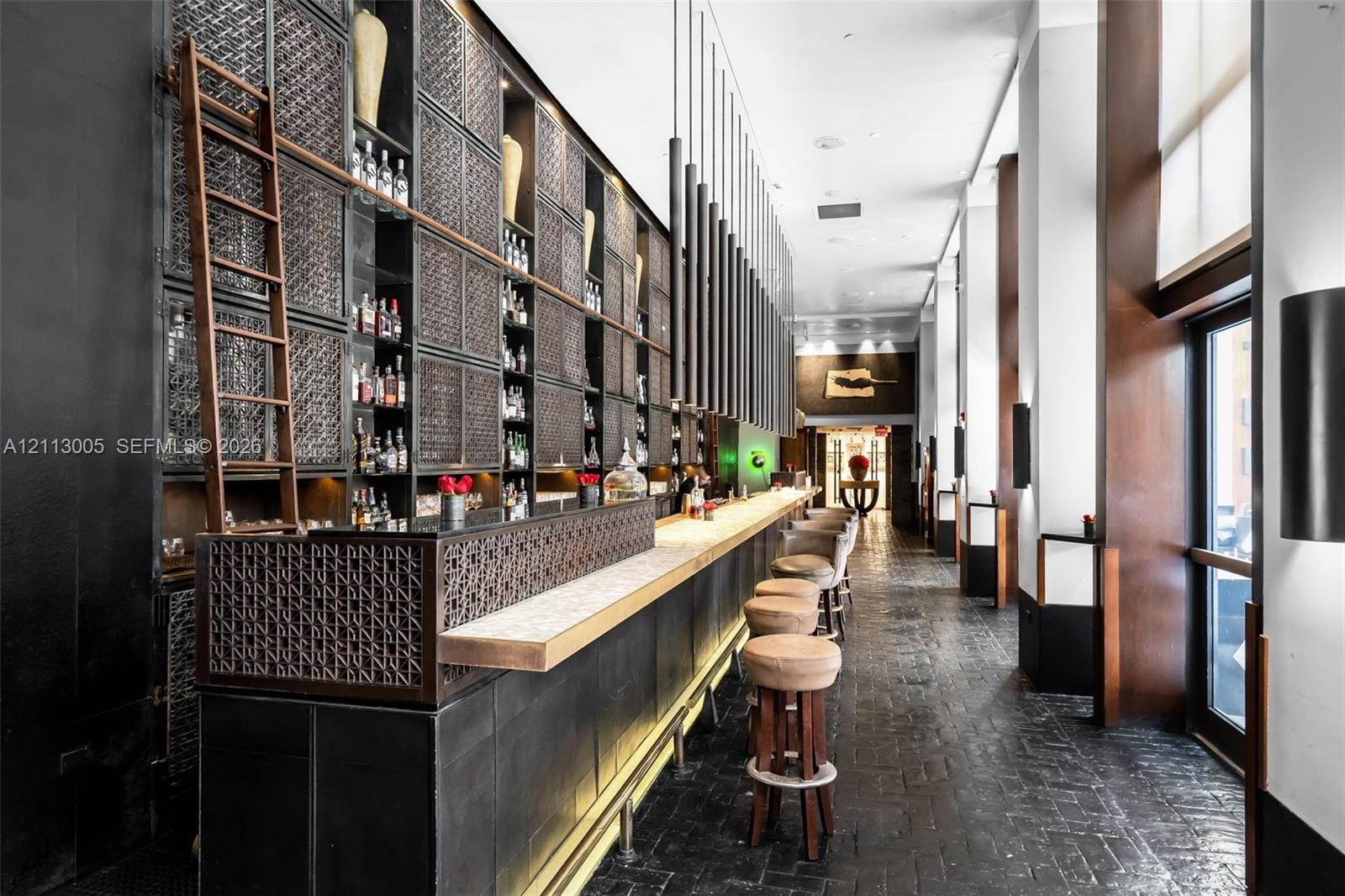 Custom bar area featuring full-height floor-to-ceiling display shelving with a rolling ladder, stone countertop, intricate metalwork detailing, and te