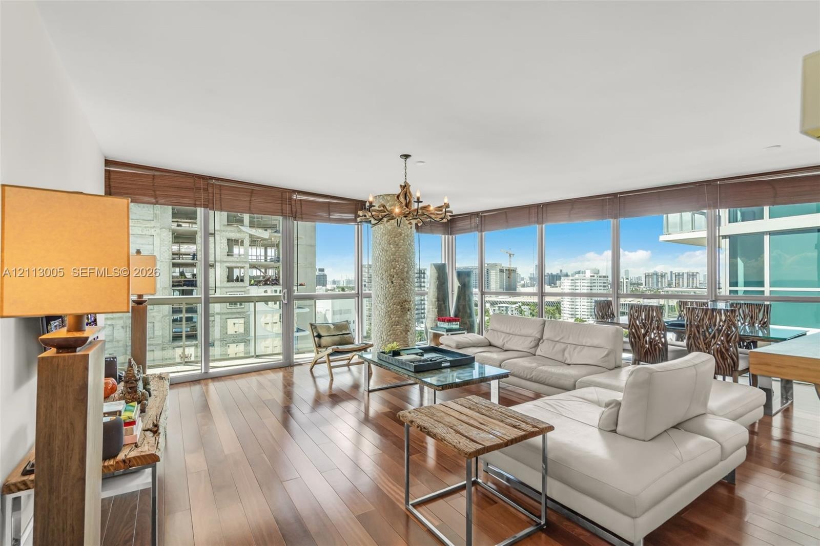 Floor-to-ceiling windows, wood-finish flooring, integrated decorative column, and multi-light chandelier