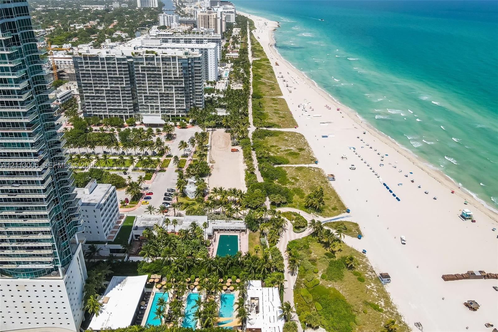Aerial perspective of a high-rise residential building featuring multiple ground-level swimming pools, manicured palm landscaping, and direct access t
