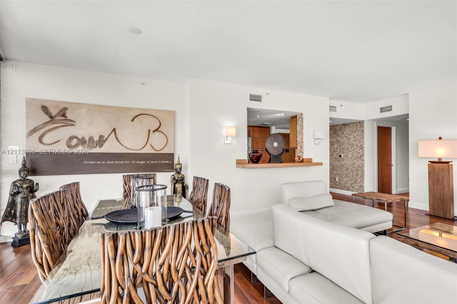 Open-concept living space featuring wood-finish flooring, a pass-through kitchen window with a built-in wooden ledge, wall-mounted light fixtures, and